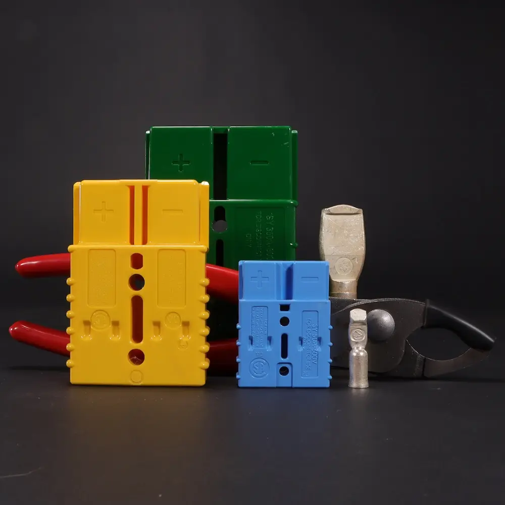 Yellow, blue, and green SY connectors (also known as Anderson connectors) with a tip and Polar Wire's tip release tool on a black background, decorative image
